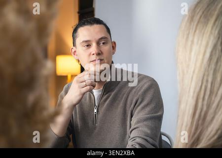 Uomo d'affari di mezza età che pensa durante la riunione, guarda al collega e analizza le informazioni. Concetto di processo decisionale, pianificazione strategica Foto Stock