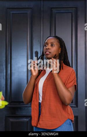 donna in piedi di fronte a una doppia porta con pannelli scuri che indossa una camicia arancione ruggine con occhiali da sole Foto Stock
