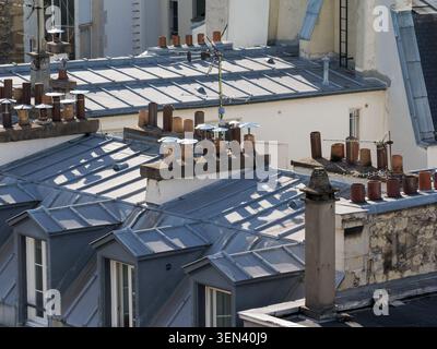 Vista dei tetti di Parigi con camini, finestre e dettagli architettonici sotto la luce del sole in Francia. Foto Stock