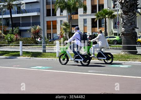 Due persone in bicicletta lungo la pista ciclabile adiacente alla Promenade des Anglais utilizzando biciclette a noleggio Lime, Nizza, Francia Foto Stock