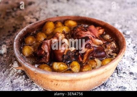 Carne e patate tradizionali balcaniche cotte lentamente sotto una campana di peka sotto le braci calde, servite in un piatto di terracotta e che mostra autentici piatti all'aperto Foto Stock