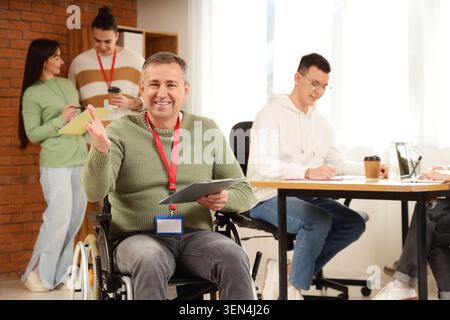 Oratore d'affari maschile in sedia a rotelle con appunti durante il seminario in ufficio Foto Stock