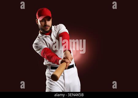 Giocatore di baseball concentrato con cappello rosso e mazza oscillante in uniforme bianca con determinazione su sfondo scuro, l'atleta dimostra potenza e determinazione Foto Stock