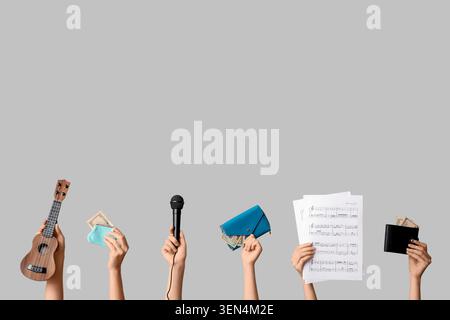 Le entrate e le spese del musicista: Mani con ukulele, microfono, portafogli e spartiti su sfondo grigio Foto Stock