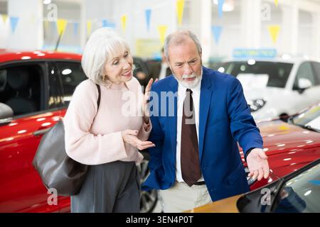 il venditore mostra un'auto a una donna anziana presso una concessionaria Foto Stock