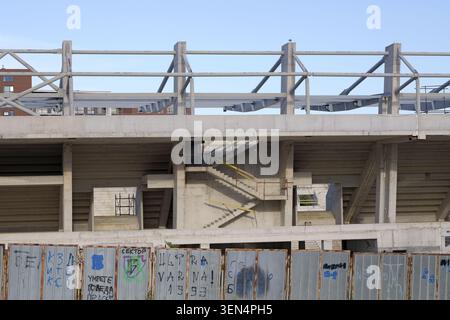 Stadio in cemento non finito con struttura a vista, stand vuoti e recinzione temporanea in metallo con graffiti cirillici, a simboleggiare lo sviluppo urbano bloccato Foto Stock