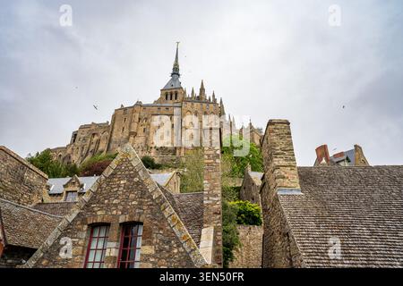 Una vista dall'angolo basso mette in risalto i tetti in ardesia e gli alti camini di pietra del villaggio di Mont Saint Michel in Normandia. Sullo sfondo, l'imponente G. Foto Stock