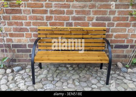 Panchina in legno di fronte a un edificio residenziale con scritte, seduta sotto la tua responsabilità, città anseatica di Wismar, Meclemburgo-Western Pome Foto Stock