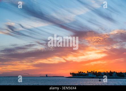 La piccola barca a vela per passeggeri attraversa l'acqua dell'oceano vicino alla sagoma scura dell'isola di Key West sotto le formazioni di nuvole viola dopo il tramonto. Foto Stock
