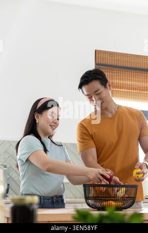 Accoppia il cesto di frutta in filo metallico sul piano di lavoro della cucina, selezionando mele e arance Foto Stock