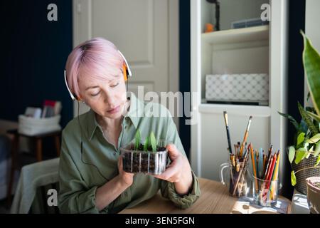 Donna matura e rilassata amante delle piante che ama il giardino interno, tenendo una scatola con piantine in crescita Foto Stock