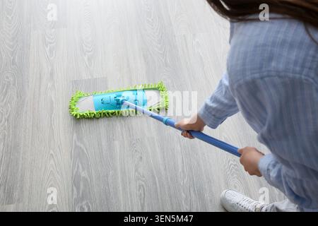 Persona che pulisce pavimenti in legno grigio chiaro con mocio in microfibra blu e verde per la manutenzione e l'igiene domestica, lo strumento di pulizia viene utilizzato attivamente per la manutenzione Foto Stock
