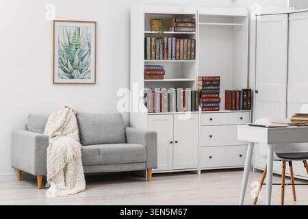 Interni moderni per l'ufficio domestico con divano grigio, librerie bianche, scrivania e opere d'arte per il lavoro e lo studio a distanza Foto Stock