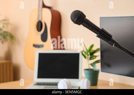 Configurazione dello studio di registrazione domestico con microfono, laptop, cuffie e chitarra acustica per la produzione musicale e il podcasting Foto Stock
