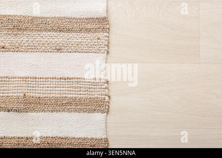 Tappeto in iuta naturale e cotone a strisce su fondo in legno chiaro con spazio per copie, il tessuto presenta una striscia bianca e beige alternata Foto Stock