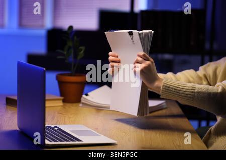 Persona che tiene una pila di documenti con un laptop sulla scrivania, l'amministrazione aziendale e il concetto di lavoro d'ufficio, una persona ha una grande pila di documenti bianchi Foto Stock