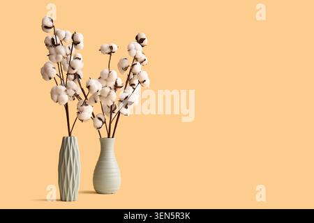 Bolls di cotone naturale in vasi decorativi su un caldo sfondo pesca, arredamento minimalista per la casa e concetto industriale tessile, il morbido cotone bianco offre Foto Stock