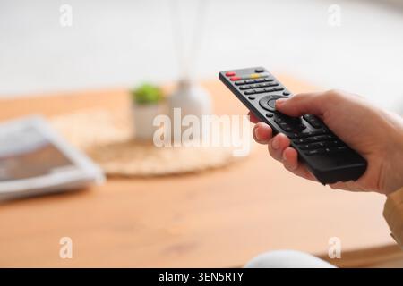 Tenendo a mano il telecomando nero per la televisione o il dispositivo multimediale, l'Home Entertainment e la tecnologia moderna, la scena suggerisce svago e convenienza Foto Stock