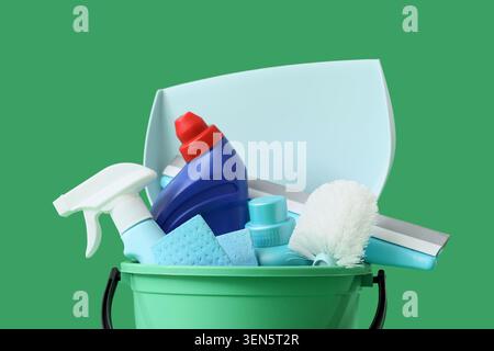 Articoli per la pulizia domestica in secchio verde con flacone spray, spugne, spazzola e flacone detergente su sfondo verde Foto Stock