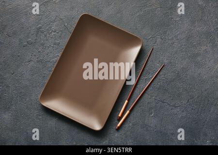 Piatto rettangolare marrone vuoto con bacchette su sfondo scuro, cucina asiatica Foto Stock
