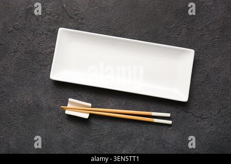 Piastra bianca rettangolare vuota in ceramica con bacchette di legno su sfondo scuro, vista dall'alto per la presentazione degli alimenti Foto Stock
