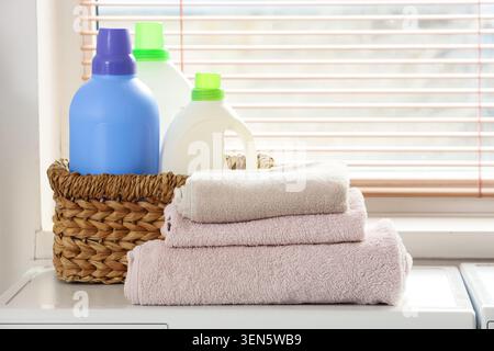 Lavare gli indispensabili per la giornata con bottiglie di detergente, ammorbidente per tessuti e asciugamani piegati puliti in un cestello in vimini Foto Stock