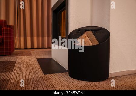 Moderno caminetto con portabicchiere nero e legna da ardere, accogliente design degli interni del soggiorno, riscaldamento e comfort Foto Stock