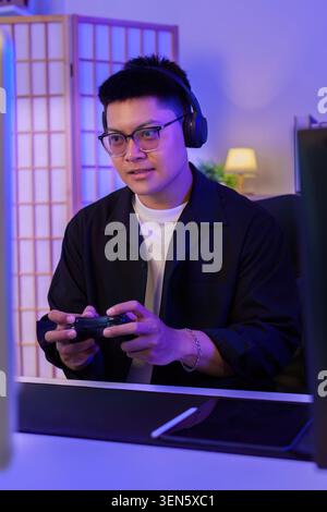 Uomo asiatico che gioca ai videogiochi con controller e cuffie per l'intrattenimento con tecnologia eSport Foto Stock