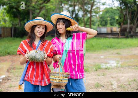 Donna cappello contadino zucca vegetale cesto di cetrioli giardino rurale sorridente, due donne asiatiche che indossano un cappello di paglia e una camicia colorata che tiene dentro il raccolto fresco Foto Stock