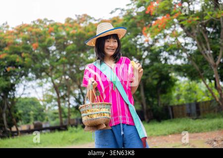 Cappello da cestino donna giardino rurale abbigliamento tradizionale sorridente albero all'aperto, donna sorridente che indossa abiti tradizionali e cappello di paglia che regge il cesto intrecciato Foto Stock