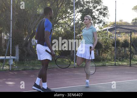 Partner di tennis ricreativi in piedi su un campo in terra battuta con racchette, donna in equilibrio su una gamba Foto Stock