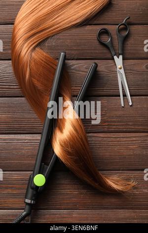 Strumenti per l'acconciatura con ciocca marrone rossastro su sfondo in legno scuro per creare concetti di bellezza e salone, piastra per capelli, forbici Foto Stock