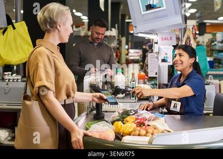 Donna di mezza età con diabete che paga per la spesa al supermercato Foto Stock