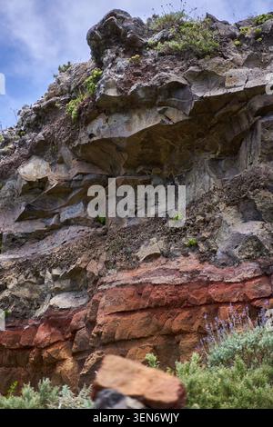 Parete rocciosa vulcanica stratificata con depositi lavici a strati e cavità erosive a Roque de Taborno, Anaga, Tenerife Foto Stock