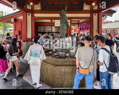 Tokyo, Giappone - 28 aprile 2026: I visitatori si riuniscono intorno alla fontana di purificazione del bronzo al tempio senso-ji di Asakusa, eseguendo la pulizia tradizionale Foto Stock