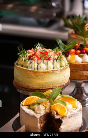 Primo piano di torte artigianali su banchi, con una torta di fragole matcha e una torta all'arancia affettata. Foto Stock