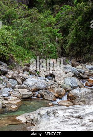 Sanzhan Creek a Hualien, Taiwan. Grandi massi grigi riempiono il letto del fiume. L'acqua limpida scorre attraverso la valle. La lussureggiante foresta verde copre le pendici. Foto Stock