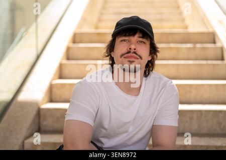 Giovane uomo di 25 anni seduto sulle scale di un complesso moderno. Foto Stock