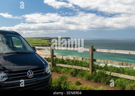 La silhouette di un camper da una rustica recinzione marrone che si affaccia sulla lussureggiante costa verde e sull'oceano Atlantico blu nell'Irlanda del Nord, Regno Unito. Foto Stock