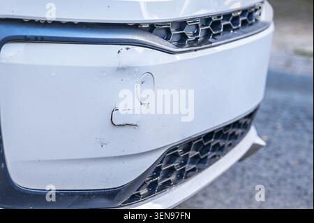 Paraurti anteriore dell'auto bianco danneggiato con graffi di vernice staccata e sensore di parcheggio Foto Stock