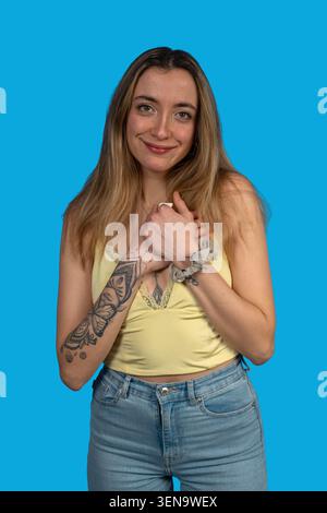 Giovane donna sorridente di apprezzamento, le mani si aggrappavano sul cuore su sfondo blu Foto Stock