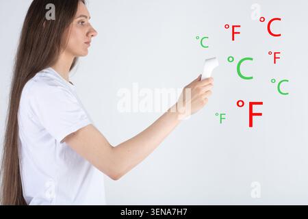 Donna che esegue un controllo medico automatico con un termometro senza contatto, confrontando temperature normali e elevate Foto Stock