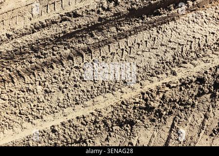 Cingoli pneumatici profondi premuti nel terreno sabbioso su strada sterrata. Fondo stradale accidentato per la guida fuoristrada di veicoli pesanti e per il trasporto rurale. Foto Stock