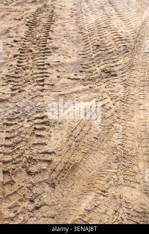 Segni di profondità del battistrada provenienti da attrezzature per l'edilizia o da un caricatore pesante. Consistenza dei cingoli degli pneumatici su sabbia bagnata e terreno fuoristrada. Orientamento verticale. Foto Stock