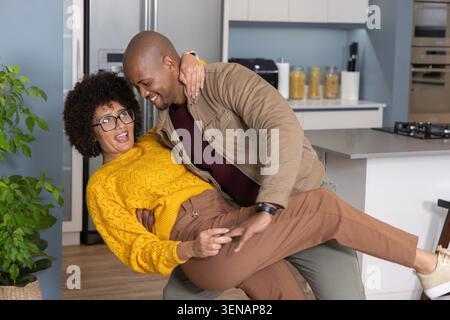 Diverse coppie che ballano, uomo che solleva una donna in maglione giallo vicino all'isola bianca in cucina Foto Stock