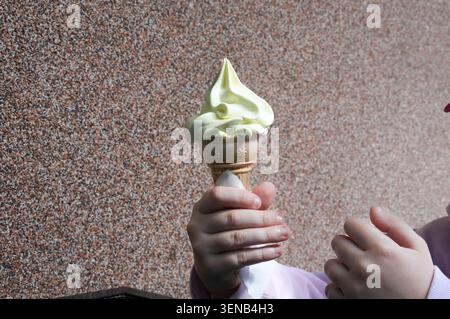Una mano di bambino che tiene un cono di gelato su uno sfondo marrone Foto Stock