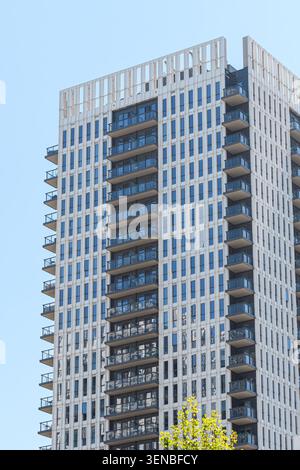 Moderno grattacielo residenziale con una facciata bianca, balconi in vetro e finestre riflettenti su un cielo blu chiaro. Foto Stock