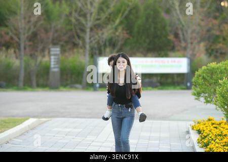 Una giovane donna cammina a piedi nudi lungo un sentiero lastricato. I suoi ricci scuri scorrono dolcemente mentre si muove in avanti. Le mani con i guanti afferrano la giacca mentre si muove dolcemente. Giallo Foto Stock