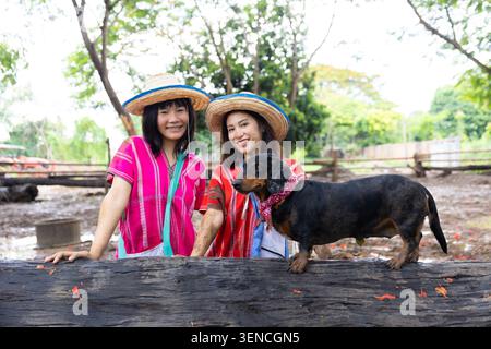 Cappello di paglia per cani da donna, bambino, panchina del parco all'aperto, abbigliamento tradizionale, animale, due persone che sorridono, cappello di paglia e colorato vestiario tradizionale Foto Stock