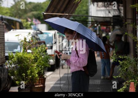 BANGKOK, THAILANDIA - 23 MAGGIO 2026: Donna che tiene l'ombrello e utilizza lo smartphone, profilo laterale, Tha Tian Foto Stock